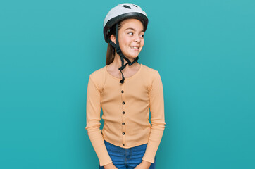 Beautiful brunette little girl wearing bike helmet looking away to side with smile on face, natural expression. laughing confident.