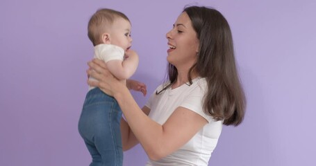Nice cheerful caucasian family isolated on purple background, young mother holding daughter in hands, smiling, looking happy. adorable child is learning world and human emotions, portrait
