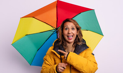 pretty middle age woman looking excited and surprised pointing to the side. umbrella concept