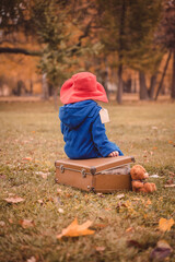 A child in a blue coat and a red hat is sitting on a suitcase. A children's photo shoot in the image of Paddington bear