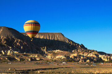 Fototapeta na wymiar Hot air balloons festival in Cappadocia. Hot air balloon flies over picturesque valley. Scenic landscape with unusual rock formation in the background. Travel and tourism concept