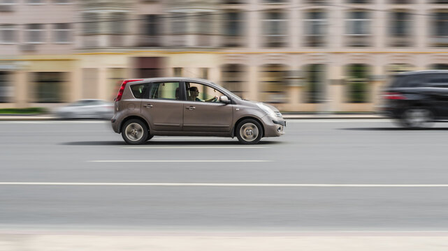 Nissan note car cruising the streets. Motion image of beige shiny hatchback running on the city road