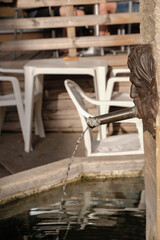 Bronze fountain with a male face on a restaurant background in the evening golden hour in Provence. Vertical image. 