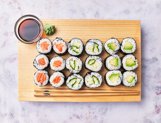  Wooden board with avocado, salmon and cucumber sushi makis on a marble surface