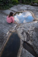 A child looking into a small pool among rocks where the sky is reflecting.
