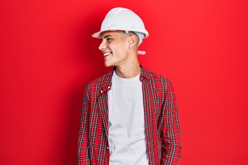Young hispanic man wearing architect hardhat looking away to side with smile on face, natural expression. laughing confident.