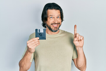Middle age caucasian man holding floppy disk smiling with an idea or question pointing finger with...