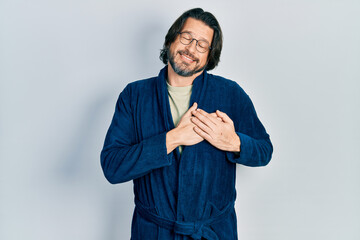 Middle age caucasian man wearing bathrobe and glasses smiling with hands on chest with closed eyes and grateful gesture on face. health concept.