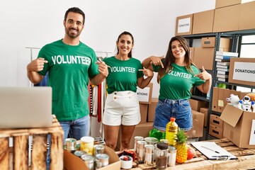Group of hispanic volunteers smiling happy pointing with fingers to volunteer uniform at charity...