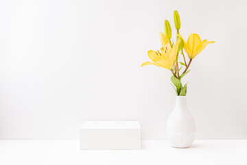 Empty white box and yellow lilies in a vase on a light background. Mockup banner for display of...