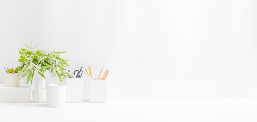 Home office desktop and branches with green leaves in a vase on a light background