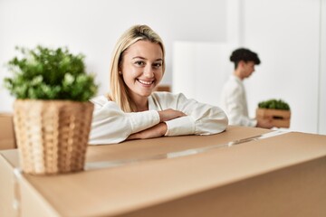 Young woman smiling happy leaning on cardboard at new home.