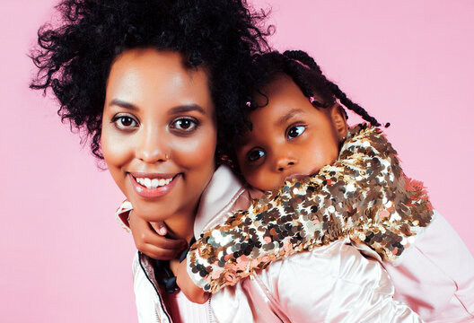 young pretty african-american mother with little cute daughter hugging, happy smiling on pink background, lifestyle modern people concept