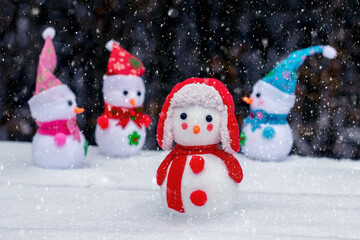 Cheerful snowmen in the woods in the snow on a dark background during a snowfall