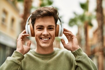 Young hispanic man smiling happy using headphones at the city.