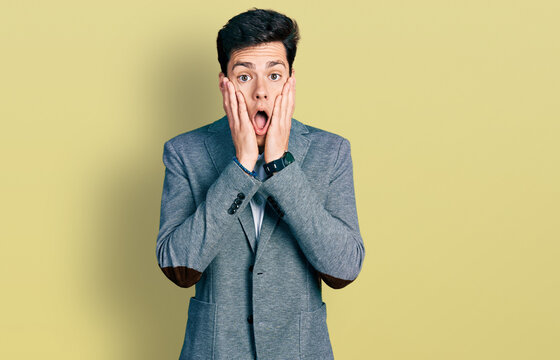 Young hispanic man wearing business clothes afraid and shocked, surprise and amazed expression with hands on face