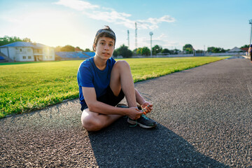 concept of sports and health - teen boy posing at a stadium track, he ties his shoelaces, a soccer...