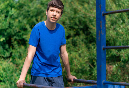 teenage boy exercising outdoors, sports ground in the yard, he does push-ups at the bars, healthy lifestyle