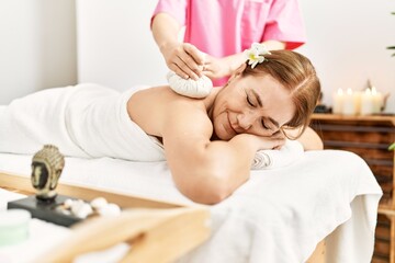 Obraz na płótnie Canvas Middle age caucasian woman having back massage using thai hot bags at beauty center