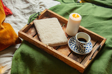 Cup of coffee and notebook with candle in tray in bed