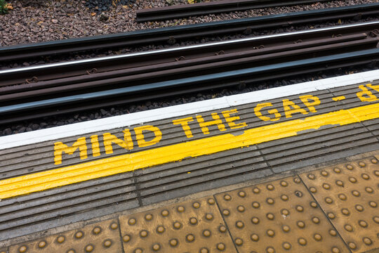 London, England, November 13th 2021:A mind the gap yellow painted floor sign. For passenger health and safety, stand away from the platform edge. Anti-slip and for the blind pavement flooring texture.