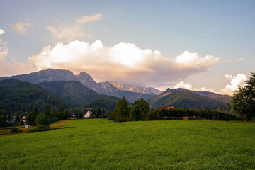 Fototapeta premium Wide angle view of a green field meadow in a countryside against giewont mountain in tatras during sunrise sunset located in Zakopane, Poland