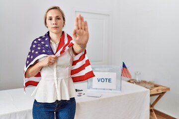 Young blonde woman at political campaign election holding usa flag with open hand doing stop sign...