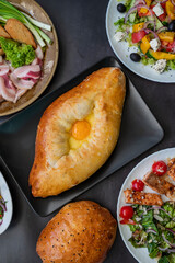 top view of khachapuri dish with cheese and egg in Adjarian with Caesar and Greek salads with potatoes and herring on the table