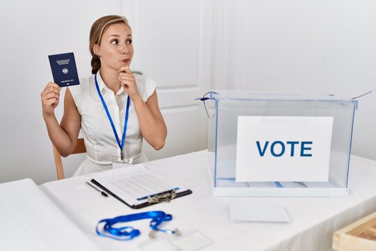 Young blonde woman at political campaign election holding germany passport serious face thinking about question with hand on chin, thoughtful about confusing idea