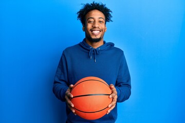 Young african american man with beard holding basketball ball smiling with a happy and cool smile on face. showing teeth.