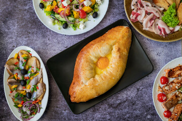 top view of khachapuri dish with cheese and egg in Adjarian with Caesar and Greek salads with potatoes and herring on the table
