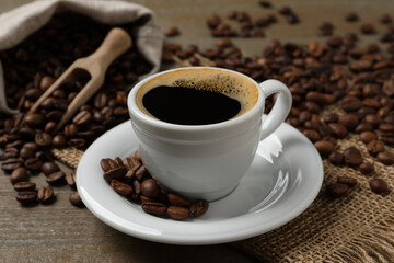 Cup of aromatic hot coffee and beans on wooden table