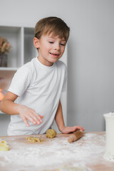 Home cooking. A child boy is engaged in cooking cookies, smiles, he is happy.