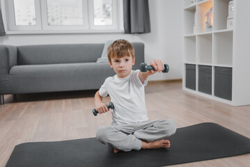 Home workout. Portrait of a boy exercising with dumbbells while sitting on the living room floor.
