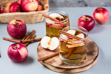 Fresh organic apple cider with cinnamon in glasses and apples on a gray background. Warming winter...