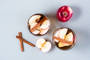 Fresh organic apple cider with cinnamon in glasses and apples on a gray background. Warming winter drinks. Top view