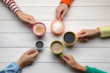 People holding different cups with aromatic hot coffee at white wooden table, top view