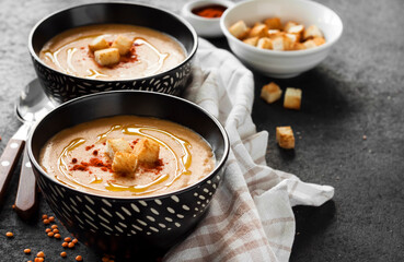 Lentil cream soup with paprika and crouton in black ceramic bowls