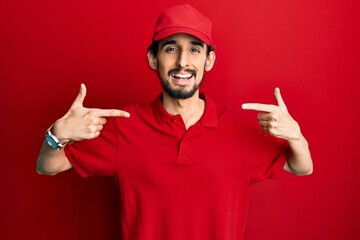 Young hispanic man wearing delivery uniform and cap looking confident with smile on face, pointing oneself with fingers proud and happy.