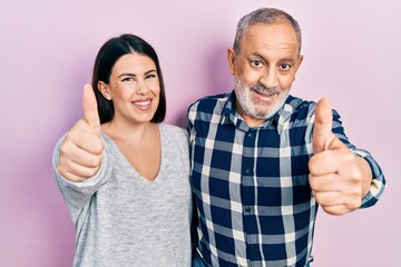 Hispanic father and daughter wearing casual clothes approving doing positive gesture with hand, thumbs up smiling and happy for success. winner gesture.