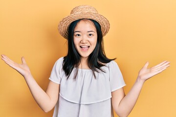 Young chinese girl wearing summer hat celebrating victory with happy smile and winner expression with raised hands