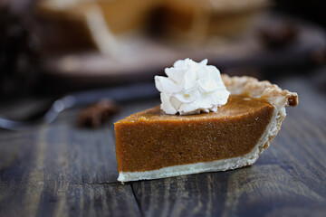 A slice of fresh baked pumpkin pie over wood background. Extreme selective focus on whipped cream with blurred foreground and background.