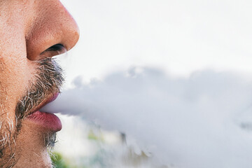 bearded man lets smoke out of his mouth, man smokes hookah outdoors, not healthy lifestyle, close-up