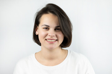 A cute, sincerely smiling girl with short dark hair in a T-shirt in a studio photo.