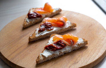 Healthy toast with salmon, sun-dried tomatoes and soft cheese on toasted bread for breakfast or lunch. Healthy snack, keto diet or dieting concept. Recipe of tasty canapes for everyday cooking.