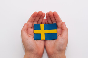 Swedish flag made of plasticine in children's hands on a white background