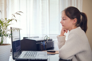 A young girl listens attentively and looks at the screen - online communication through a laptop at home or at work