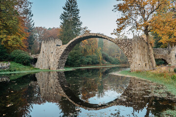 Unique looking bridge Rakotzbrucke,also called Devils Bridge,Saxony,Germany.Built to create circle when it is reflected in waters.Colorful fall landscape.Fantastic autumn foliage.Amazing place