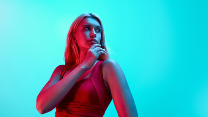 Closeup portrait of attractive blond sports girl in red sportswear on bright neon cyan background....