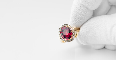 Golden ring with rhodolite gem and diamonds in jeweler hand in a white glove. Copy free space on...